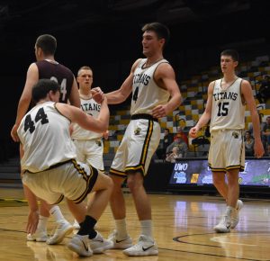 Jack Flynn (44) is helped off the hardwood by Brett Wittchow (4) after hustling for a loose ball late in the game against UW-La Crosse. The Titans squeaked out a win against the Eagles to move on to the semifinals of the WIAC playoffs.
