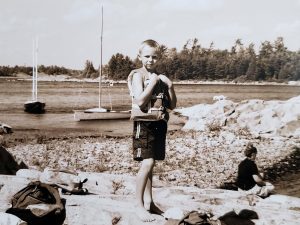 A very young Owen standing in the water with a life vest on him