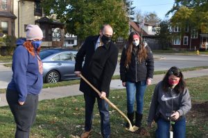 Chancellor Andrew Leavitt shovels dirt into the Ratzburg apple tree sapling hole while Lisa Mick supports the sapling.