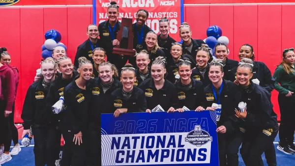 Courtesy of UW-Oshkosh Athletics -- UWO gymnastics poses for a photo with the 2026 NCGA championship trophy and signage on March 20.